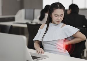 office woman sitting and holding her lower back pain or having problem with part of body backache after working on computer too long time in office.